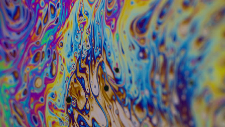 Vivid rainbow color. Iridescent surface. Defocused purple green liquid oil paint curve acrylic slick on abstract dark black blurred light art background.