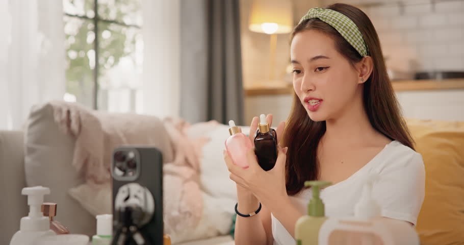 Asian woman beauty influencer, content creator filming skincare product review on smartphone at home. Gen Z lifestyle social media trends. digital marketing, promotions, cosmetic branding vlogs.