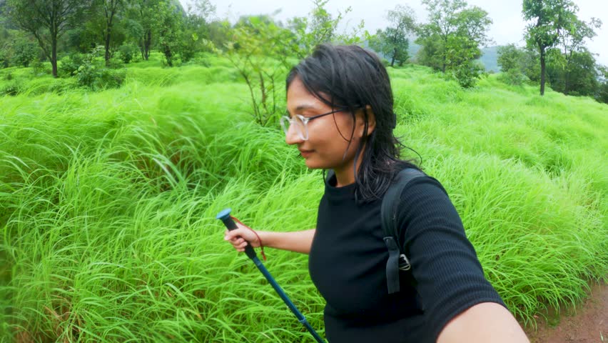 A Young Woman Hiking Through the Wilderness at Sahyadri hills, Maharashtra, India. Concept of adventure spirit and love for nature. Monsoon trekking. Female Hiker with Backpack in Lush Green Forest