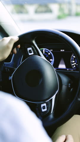 Vertical Format Video of Unrecognizable person's hands holding steering wheel while driving modern electric car on the street road. Confident man driving expensive car. Driver Turning Steering Wheel