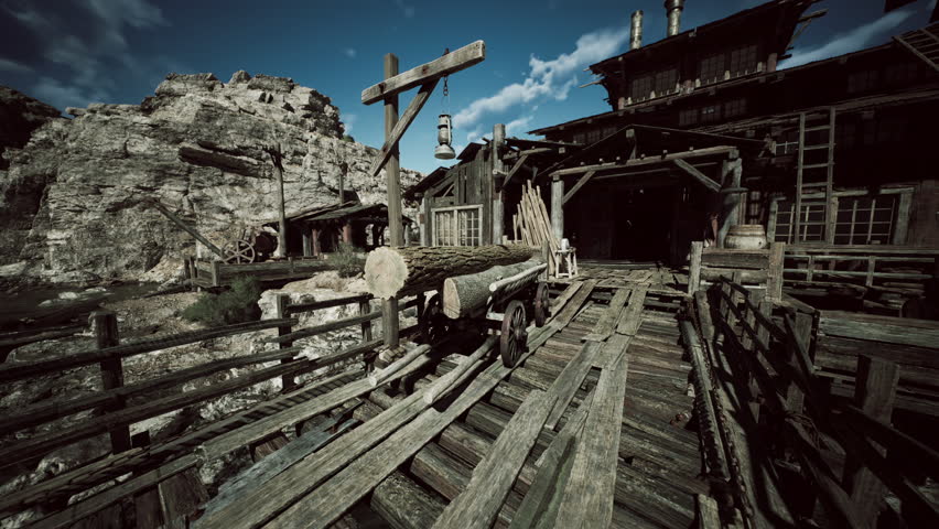 A rustic wooden bridge leads to an old building, surrounded by rocky terrain. Logs are stacked nearby, and a lantern hangs above, creating a picturesque setting.