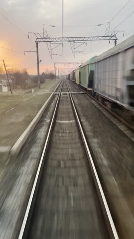 Motion blur view of railroad tracks at sunset with a freight train passing on the right, captured from the rear of a moving train. High quality 4k footage