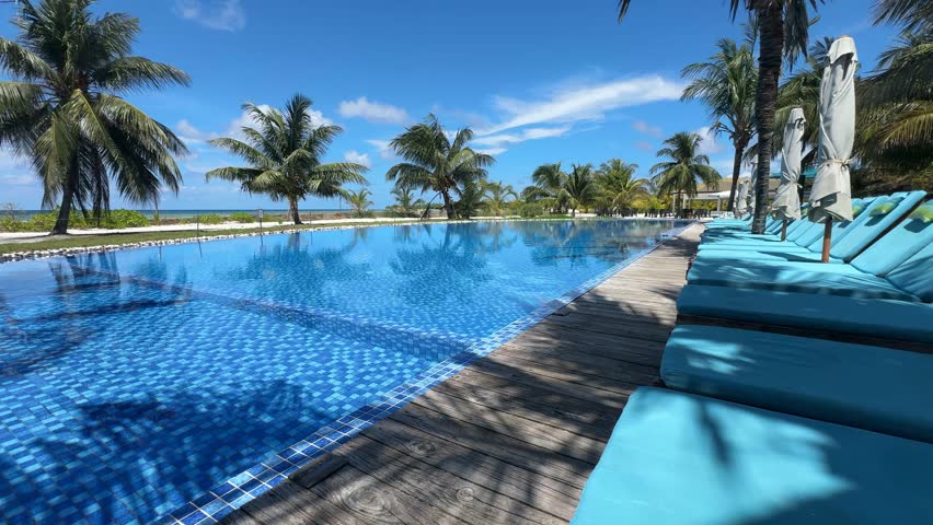  Elegant infinity pool at a luxury tropical resort with turquoise loungers, closed umbrellas,lush palm trees, and breathtaking ocean view on a warm and sunny summer day — the perfect setting for relax