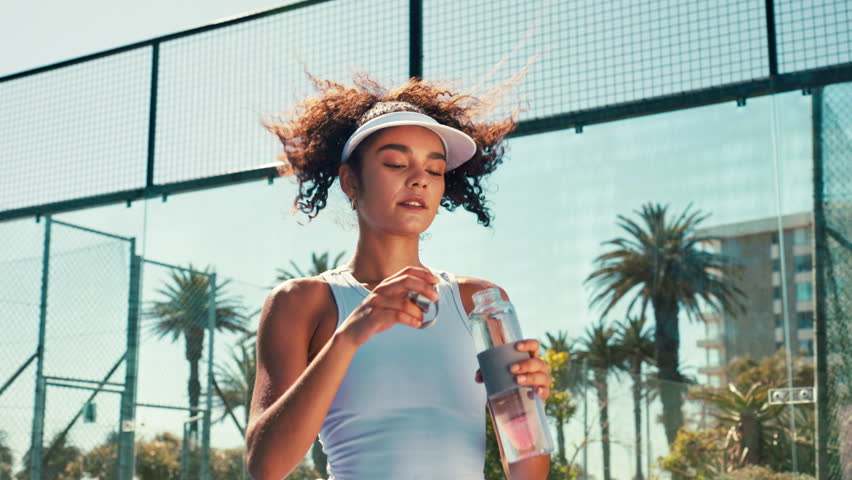 Tennis player, woman and drinking water on court for match recovery, workout hydration and practice break. Padel sports, athlete and liquid bottle for fitness refresh, thirsty or resting for wellness