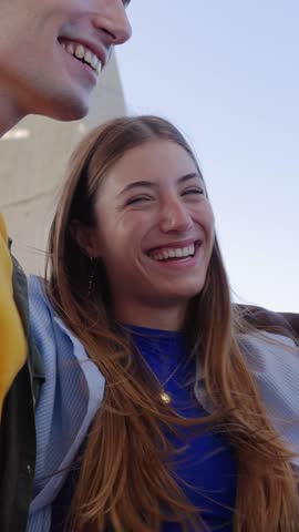 Vertical HD video of young people having fun together embracing each other outdoor. Student teenage friends laughing while hanging out outside. Youth community concept.