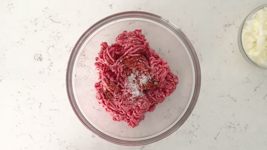 Seasoning ground beef with salt, garlic powder, and chopped onion for a flavorful mix.