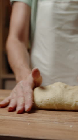 Vertical video. Person Preparing Dough on a Wooden Surface, Dough Flattened and Ready for Further Shaping or Baking Steps. Slow motion.