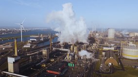 Drone footage showing a large-scale industrial complex emitting smoke, contrasted with nearby wind turbines – symbolizing the energy transition. - Powered by Shutterstock - Get 15% off with code: PIKWIZARD15
