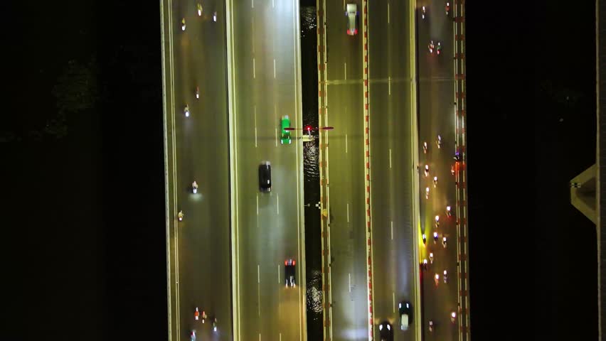 Top-down aerial view of heavy traffic on a central bridge over the Saigon River in Ho Chi Minh City, Vietnam, illuminated by city lights and billboard signs.