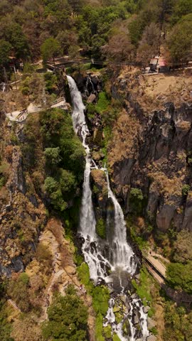 Water cascading down mountain cliffs, flowing between brown stones and lush green plants and trees.