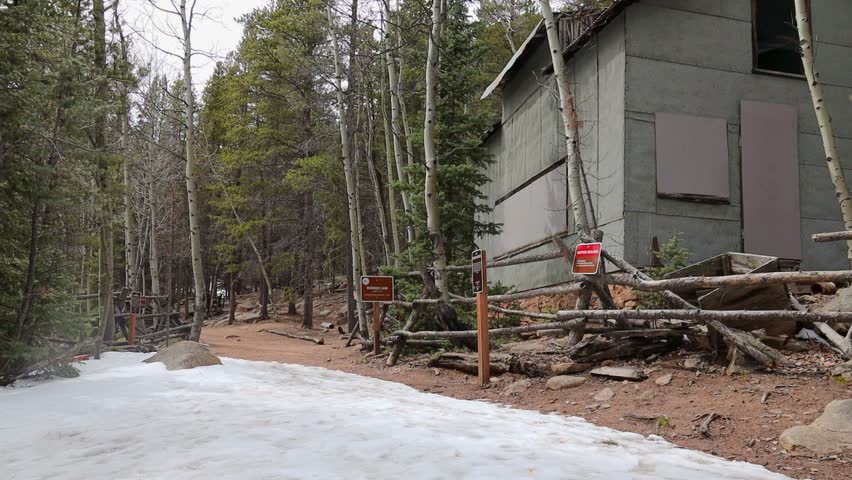 Solo male hiker walking past and stopping to examine remote abandoned buildings in the Rocky Mountains of Colorado. Filmed in Staunton State Park during the spring.