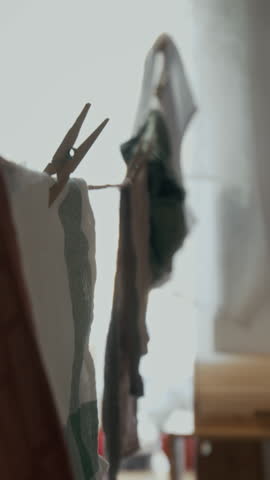Vertical shot of unrecognizable African American man hanging washed clothes on line indoors in small apartment