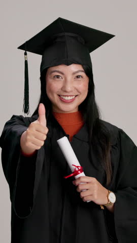 Thumbs up, smile and woman with graduation diploma at studio for success, learning goal or academic excellence. Portrait, college graduate and Asian student with like hand gesture on gray background