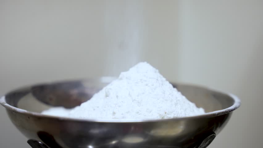 Flour being measured accurately on a kitchen scale with a spoon for baking preparation.