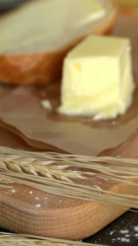 Camera movement on cut piece of butter on background of rustic products. Natural farm food. Vertical shot