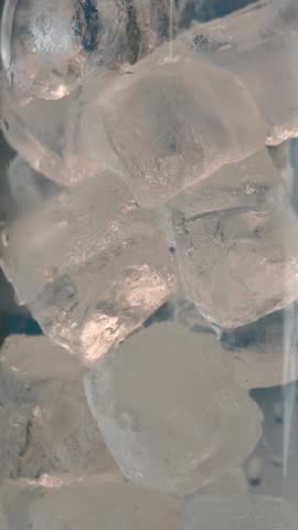 Clear sparkling drink poured over ice cubes in glass creating fresh fizz and cold bubbles in slow refreshing motion.