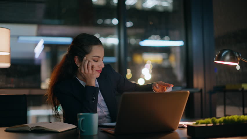 Overworked office woman rubbing eyes waiting finish of work day at late evening room closeup. Bored businesswoman flipping papers stretching at dark workplace. Tired lady at night home. Overtime job