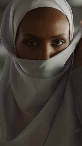 Elegant African-American woman raises up edge of hijab to hide face on embankment slow motion. Pretty Muslim lady in old town. Islamic lifestyle