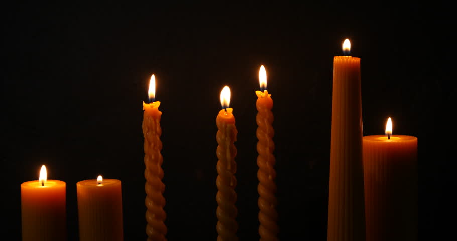 Many burning beeswax candles in darkness, closeup