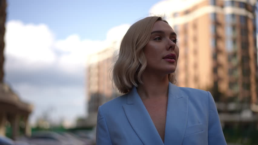 A fashionable woman dressed in a stylish light blue blazer confidently walks through a vibrant modern city