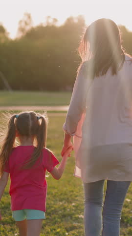 Woman with little son and daughter walk along park meadow backside view slow motion. Happy family of mother and children. Public place to rest