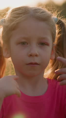 Tired little girl with ponytails waves hand to cool down in park at sunset light slow motion. Child overheated after active game. Summer season