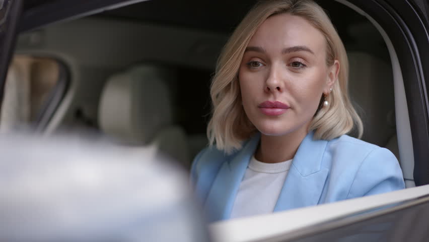 A fashionable woman enhances her appearance with lipstick while sitting in an elegant luxury car environment