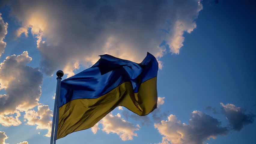 There is a beautiful view of the Ukrainian flag majestically waving in the wind against a backdrop of cloudy skies
