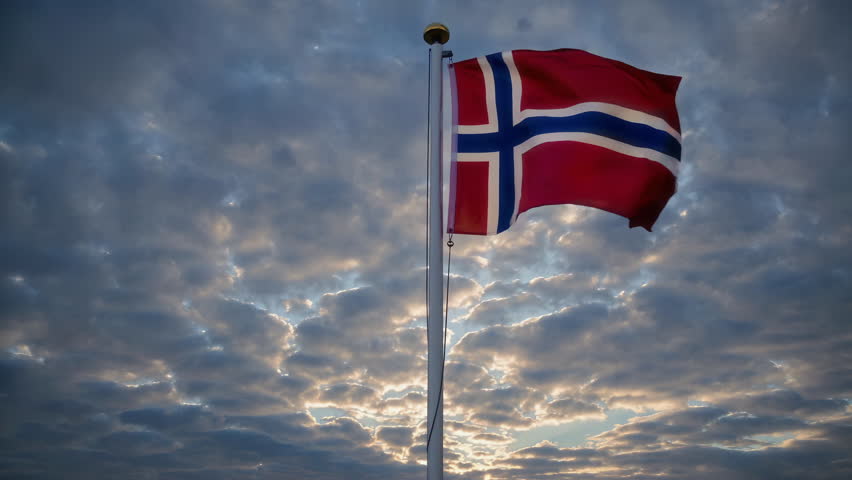The stunning Norwegian flag is waving majestically and proudly beneath a cloudy sky during a beautiful sunset