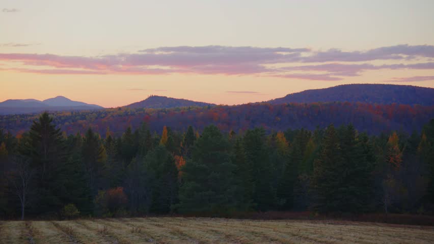 A glowing fall forest meets the fading light of day with distant mountains standing tall in this stunning 4K sunset footage near Roaring Brook Falls, full of color and tranquility.