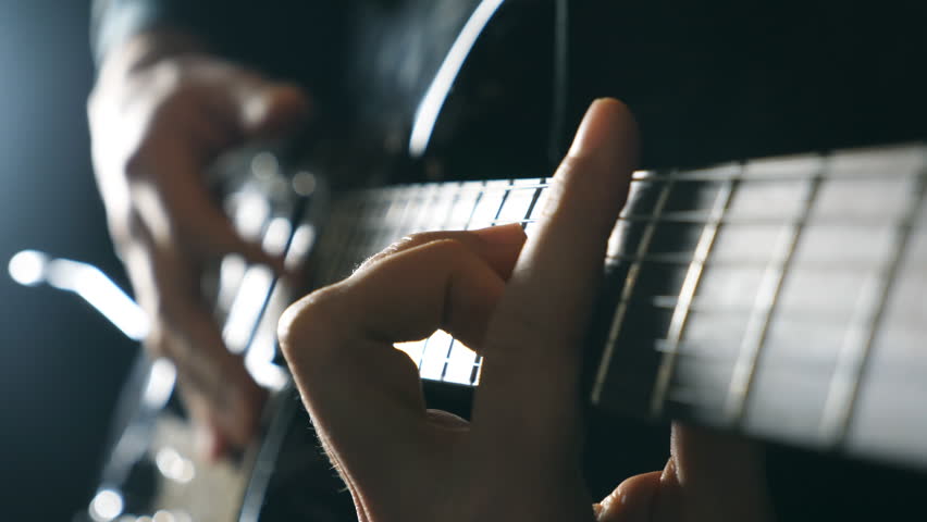 Hands of male musician playing at electric guitar. Mens arms plays solo of rock music. Close up fingers of guitarist at the strings. Beautiful black background at studio. Slow motion Close up