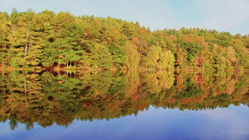 A peaceful autumn landscape featuring the vibrant colors of fall foliage reflected in a tranquil lake, filmed at Planting Fields Arboretum, Oyster Bay, NY, showcasing the beauty of the landscape.