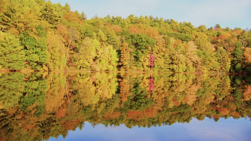 Footage of a tranquil autumn landscape with colorful fall foliage and its reflection in a calm lake, filmed at Planting Fields Arboretum, Oyster Bay, NY, during the vibrant fall season.