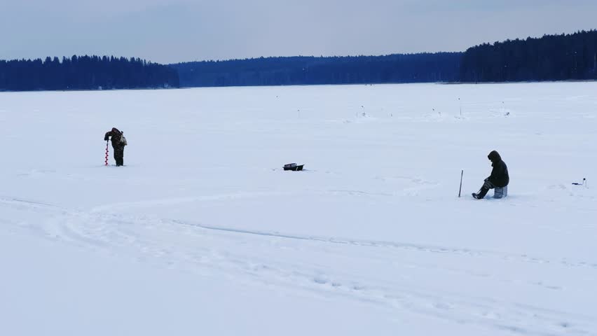 Fishermen on a winter fishing trip catch fish. Winter ice fishing. A winter fisherman is fishing on the pond. A man is sitting on the ice with a camping box, a drill and a thermos. Udmurtia. 4K