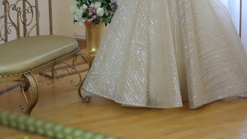 A beautiful wedding dress with a long, lace-trimmed train is displayed on a mannequin. The scene is decorated with flowers and ornate pedestals, creating a romantic atmosphere.