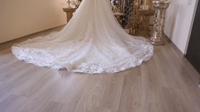 A beautiful wedding dress with a long, lace-trimmed train is displayed on a mannequin. The scene is decorated with flowers and ornate pedestals, creating a romantic atmosphere. - Powered by Shutterstock - Get 15% off with code: PIKWIZARD15