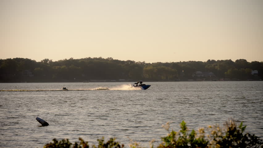 The speedboat is moving across a vibrant water. A person is being towed behind the boat, wakeboarding or water skiing, Carving through the water with a dynamic posture.