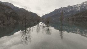 Aerial shot - Turquoise lake surface mirroring snow capped Pyrenees mountains and bare trees at tranquil Ibon de los Banos winter landscape in Huesca, Spain - Powered by Shutterstock - Get 15% off with code: PIKWIZARD15