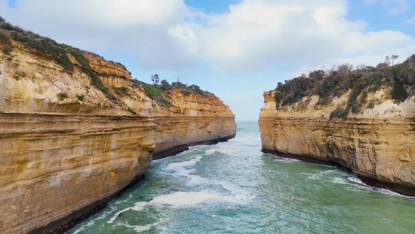 Drone footage captures the rugged cliffs and turbulent ocean at Loch Ard Gorge, Port Campbell, Australia, under bright daylight