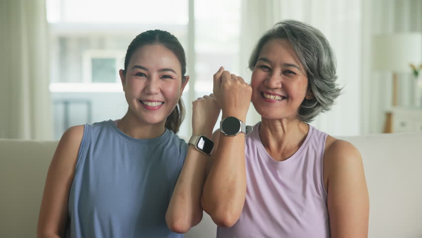 Adult child smile look at camera showing gift AI smart watch IOT app with middle age old mum. Love health care older mom asia elder people sit at home happy wear wrist trace help protect aging life.