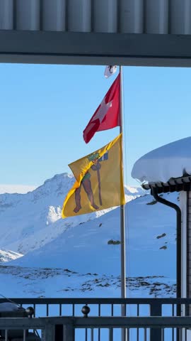 a flag of switzerland and a flag of the canton of graubunden flutter in a ski center on a sunny day