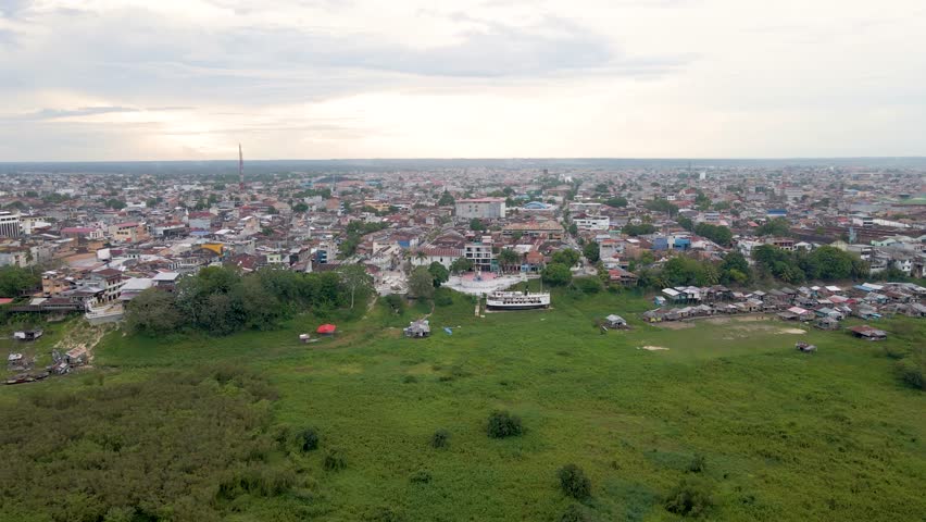 Aerial pullback Iquitos city near Pier Maldonado, Peru, with grassy fields and dense skyline behind