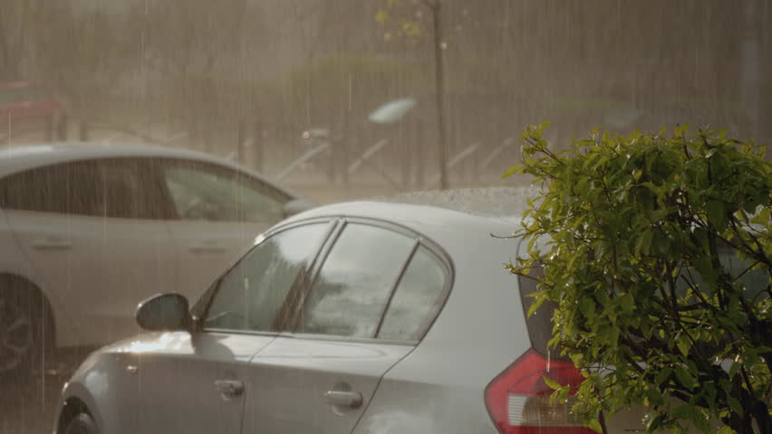 Powerful summer storm pelting parked vehicles with large hailstones, causing potential damage to car roofs and windshields during intense precipitation event