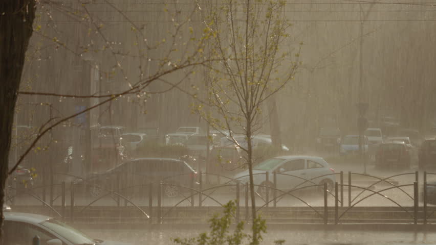 Heavy spring rainstorm creating dramatic downpour with hail falling on urban street, intense precipitation drenching parked cars and surrounding cityscape