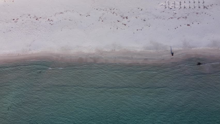 An aerial view of people walking on a white beach near the ocean in a sunny weather in Sardinia, Italy