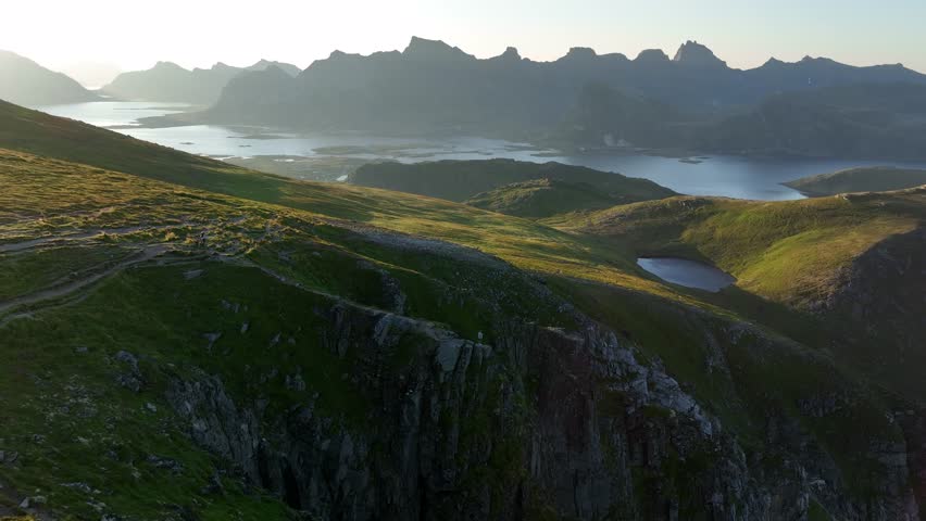 A drone view of Ryten, Lofoten Islands, Norway, showcasing rocky hills covered in lush green, with the distant sea surrounded by towering hills
