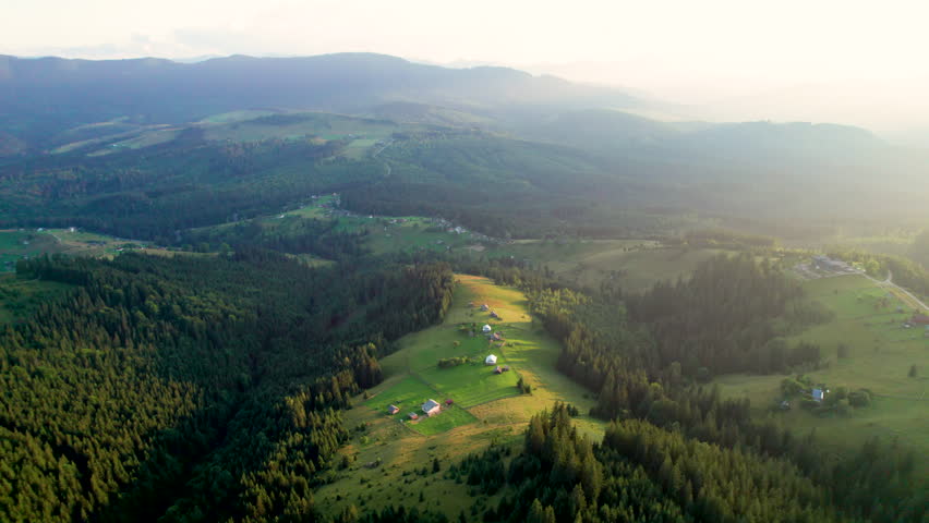 Breathtaking aerial view of mountain landscape at sunset. Golden light bathes rolling hills and lush forests, creating serene and idyllic scene. Distant mountains adding depth to picturesque vista.