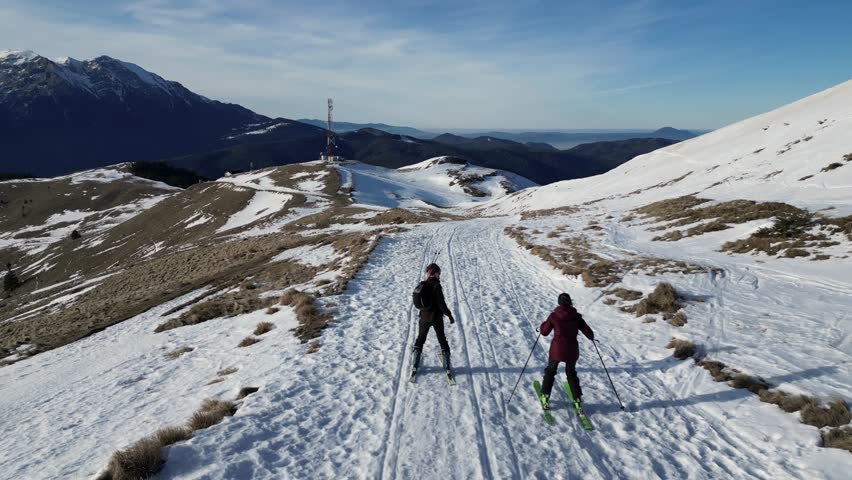 An aerial footage of a couple cross-country skiing on Bucegi Mountains in central Romania, on a sunny day