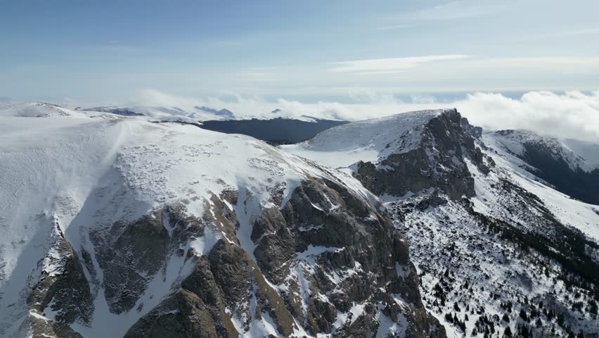 A drone view of the snow-covered Bucegi mountains of Romania during winter with rocky peaks and clear blue sky in Brasov