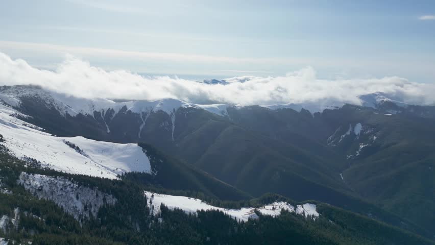 An aerial landscape view of the Carpathian Mountains with snow, low clouds and clear skies during winter in Romania
